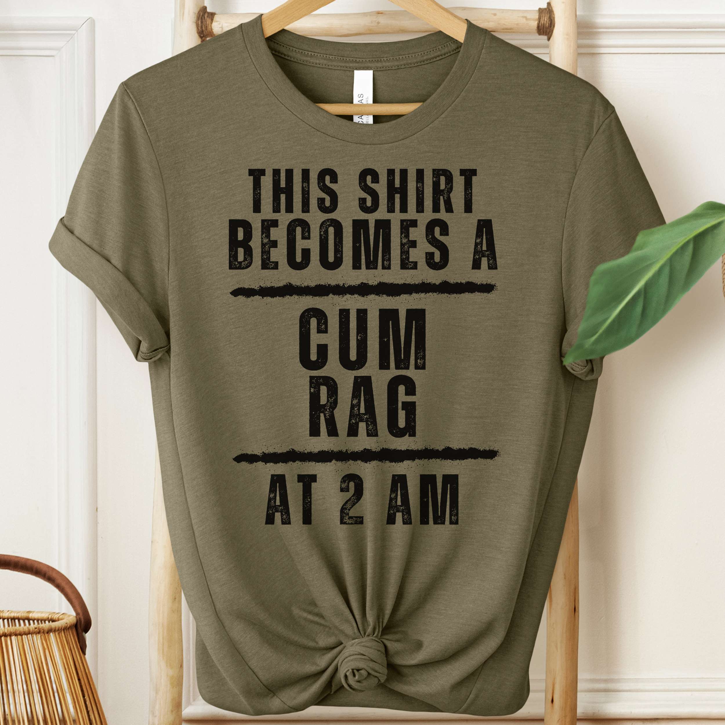 Green t-shirt with humorous text on a hanger against a white wall.
