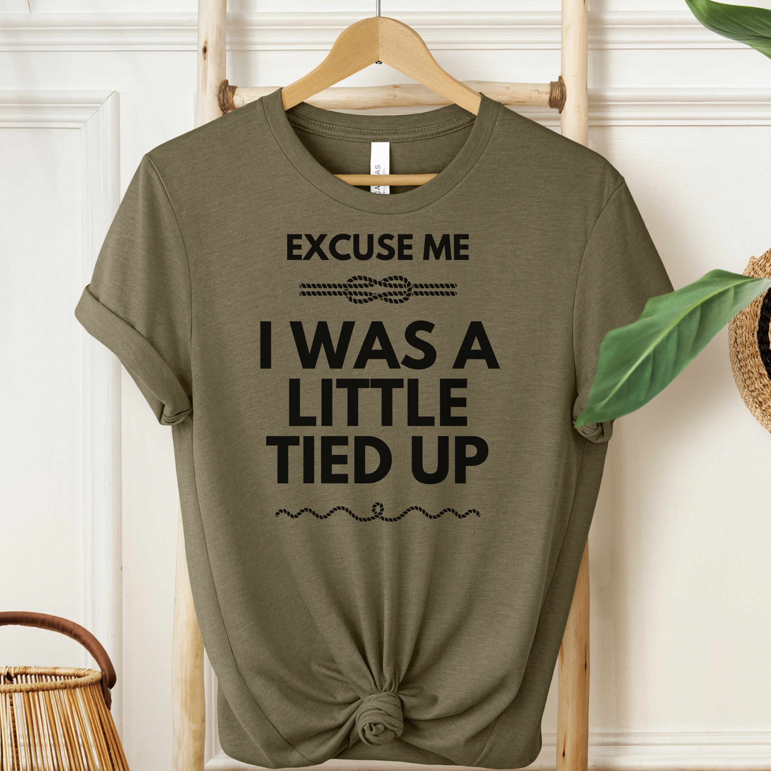 Green t-shirt with humorous text on a hanger against a white wall.