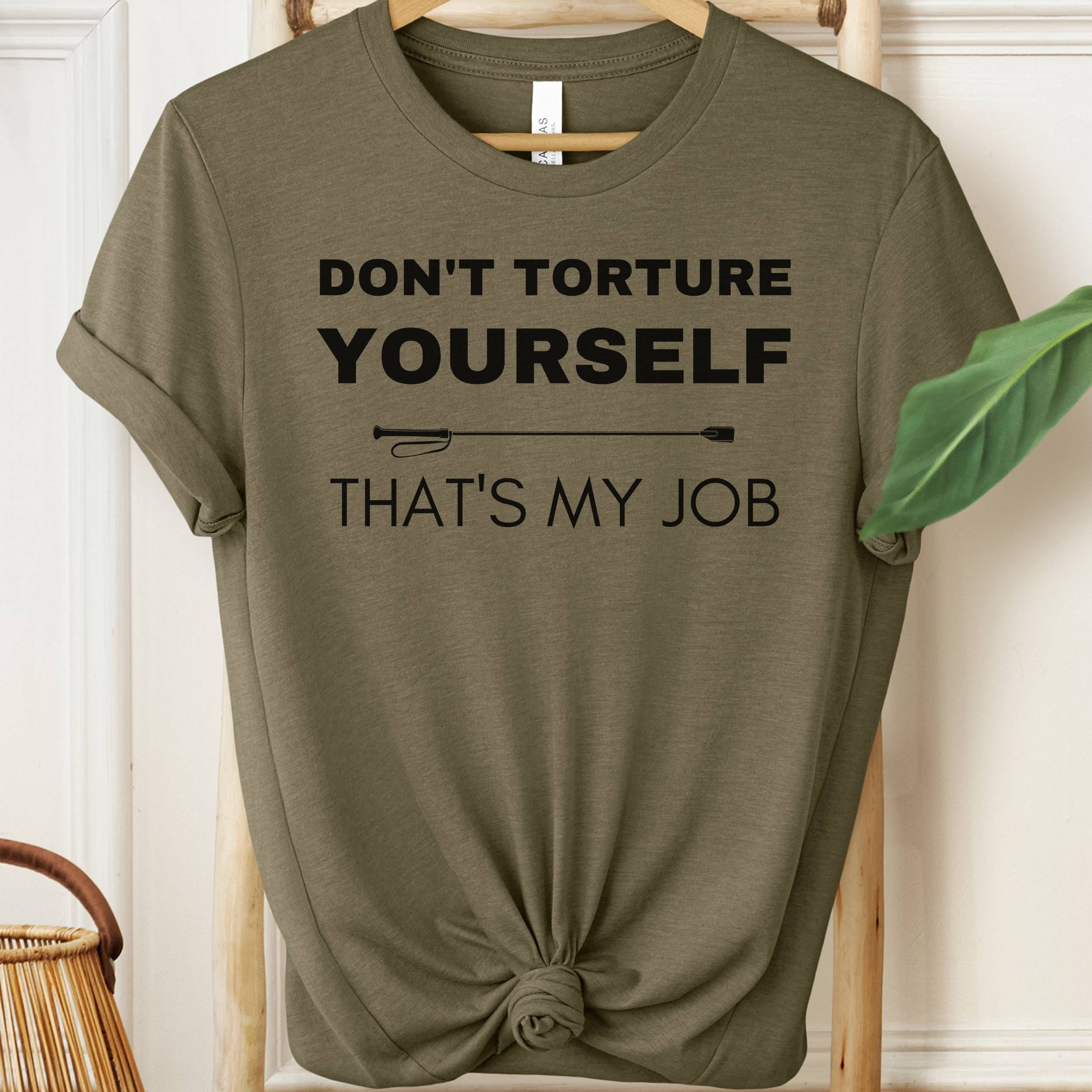 Olive green t-shirt with text 'Don't torture yourself, that's my job' on a hanger.