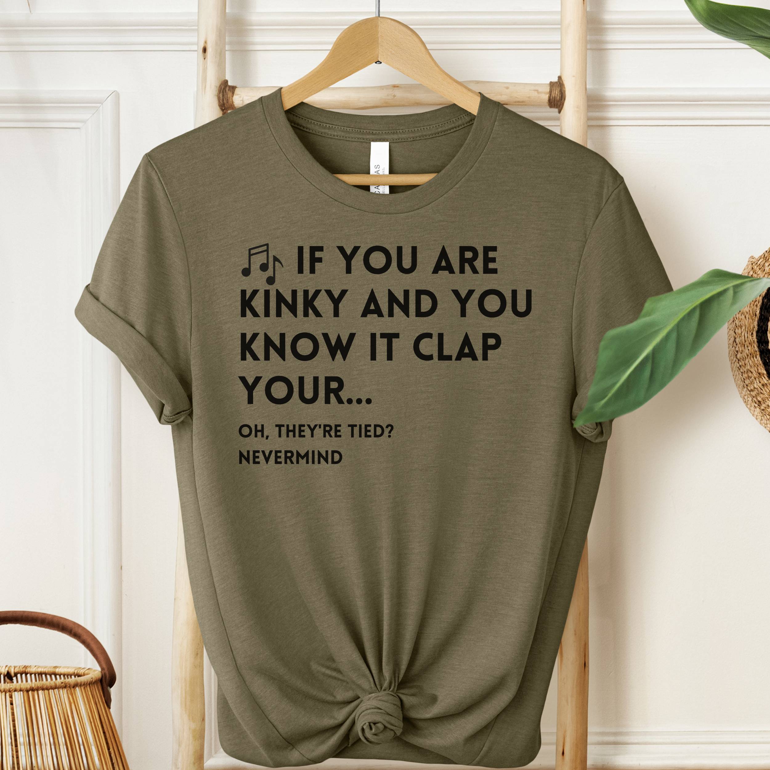 Green t-shirt with humorous text on a hanger against a white wall.