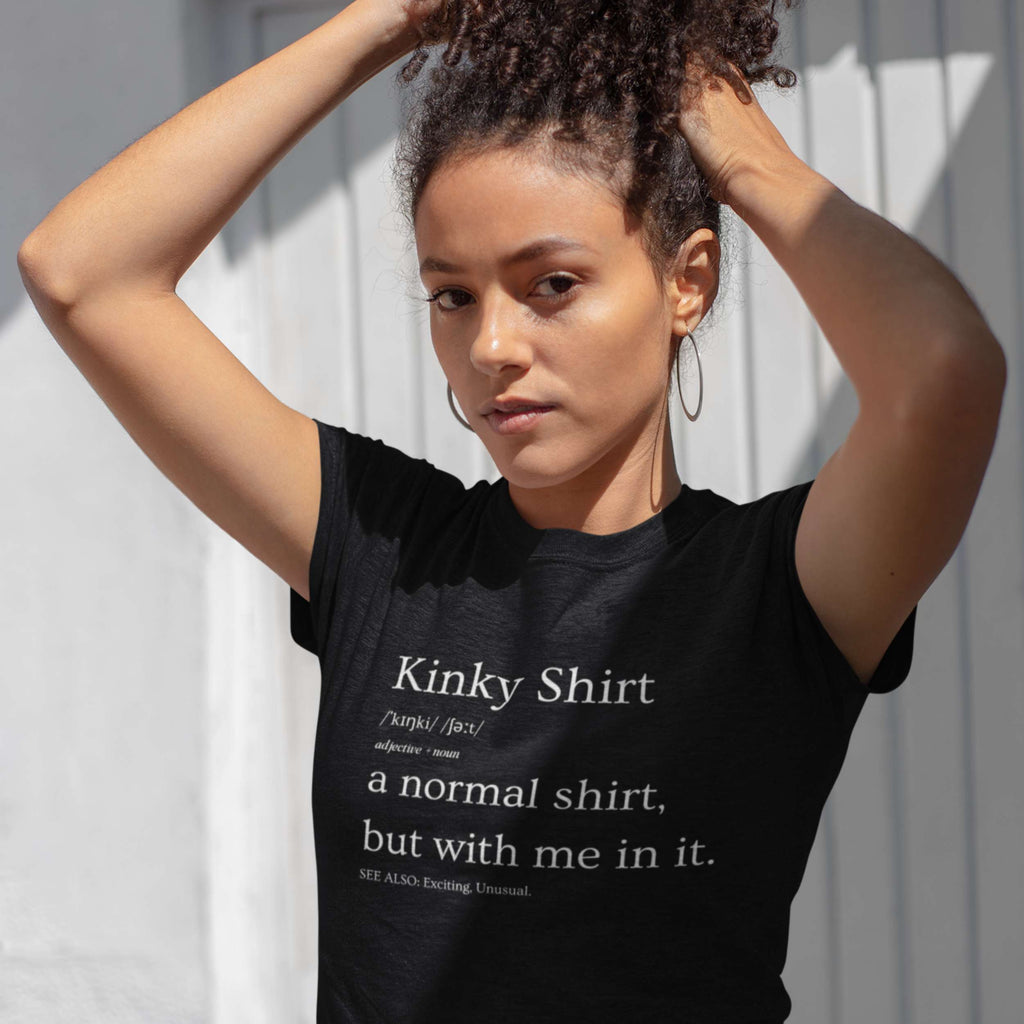 Woman wearing a black t-shirt with text, standing against a light-colored wall.