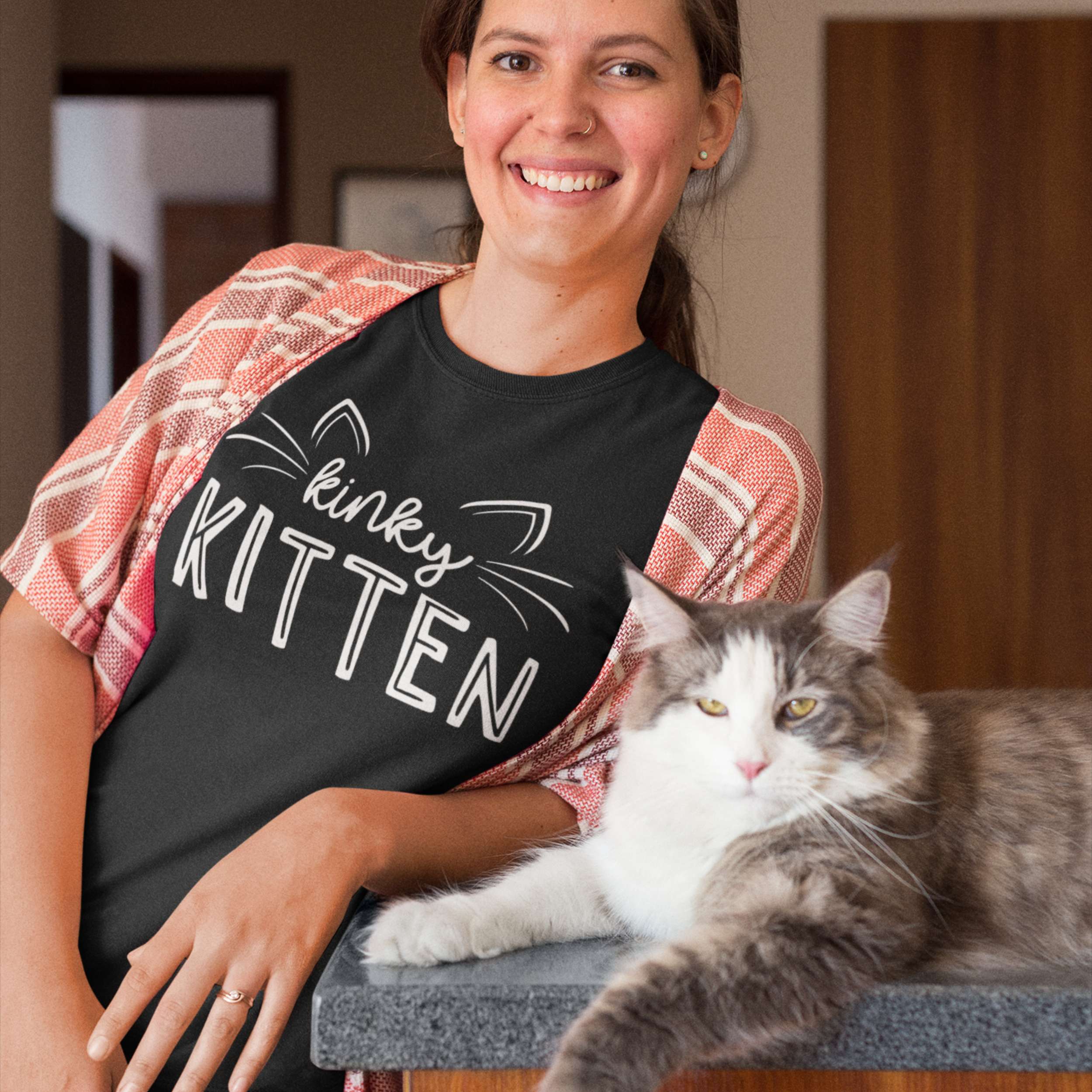 Woman wearing a black t-shirt with 'kinky KITTEN' text, sitting next to a cat.